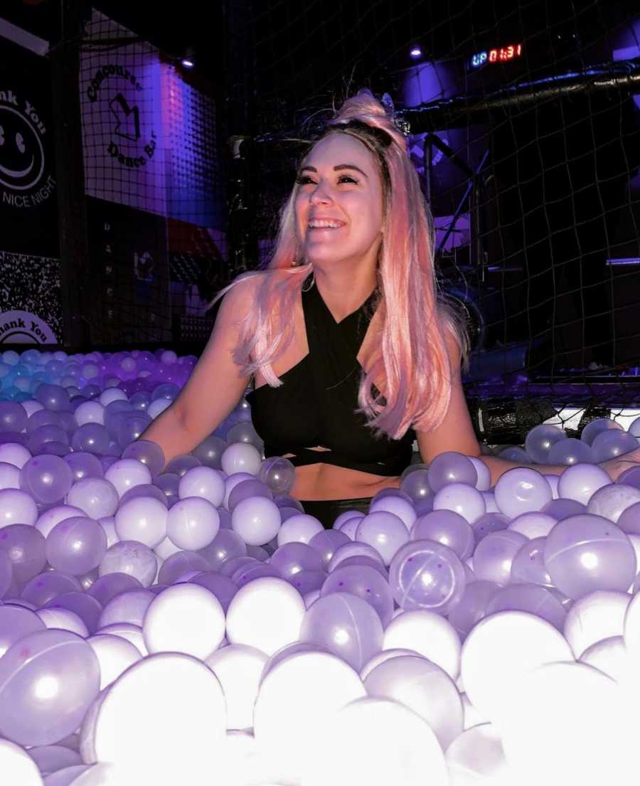 Woman standing in purple ball pit wearing pink wig