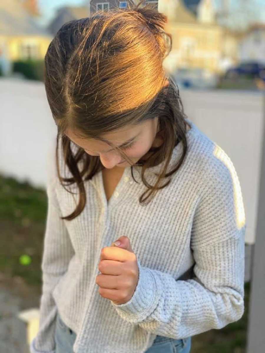 A young girl with brown hair stands looking down