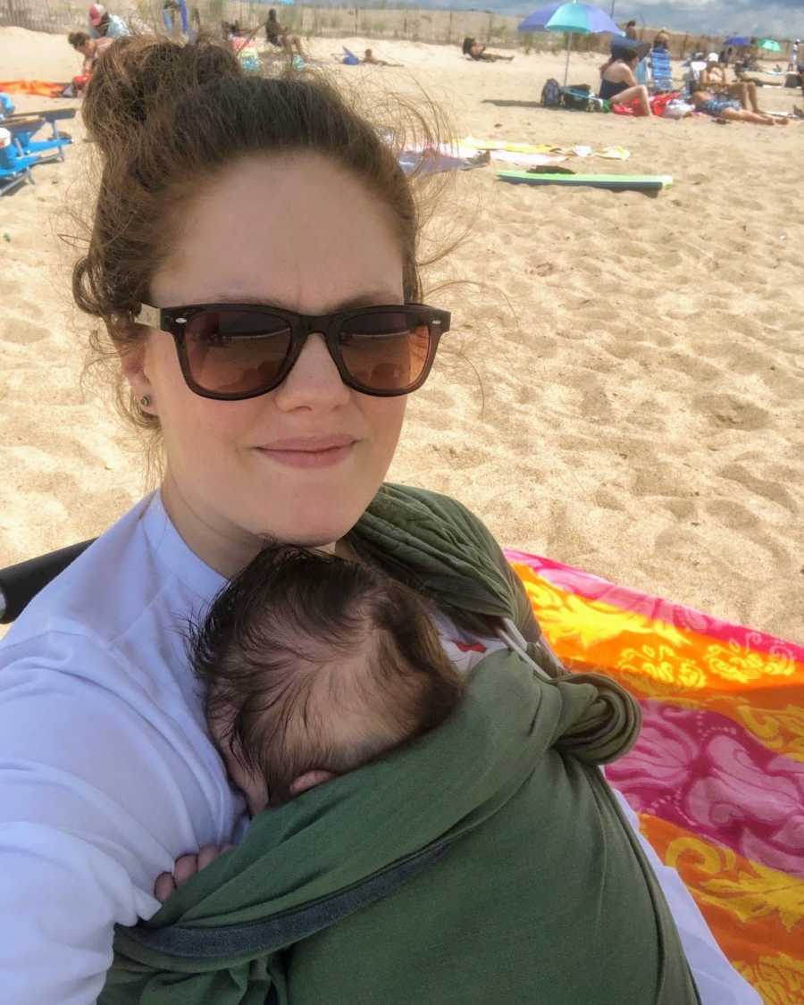 Mother holding swaddled newborn baby on sunny beach day