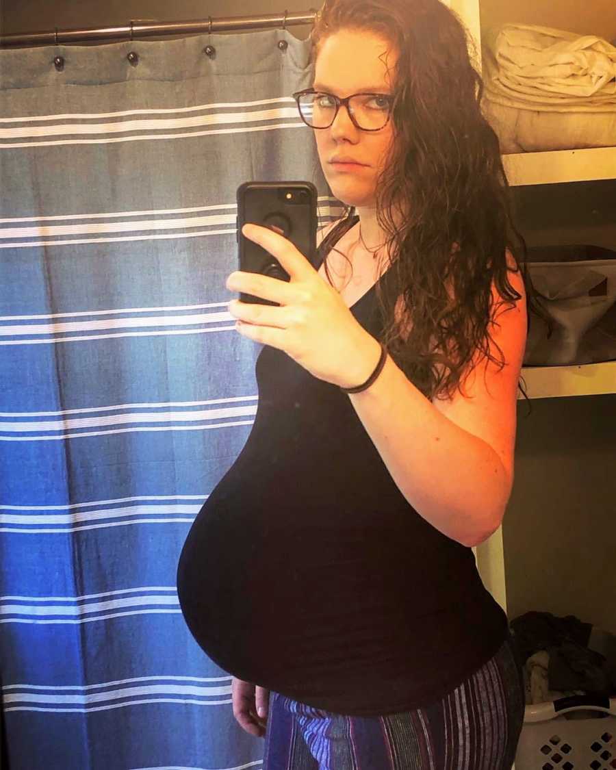 Pregnant woman wearing black tank top taking picture of baby bump in mirror