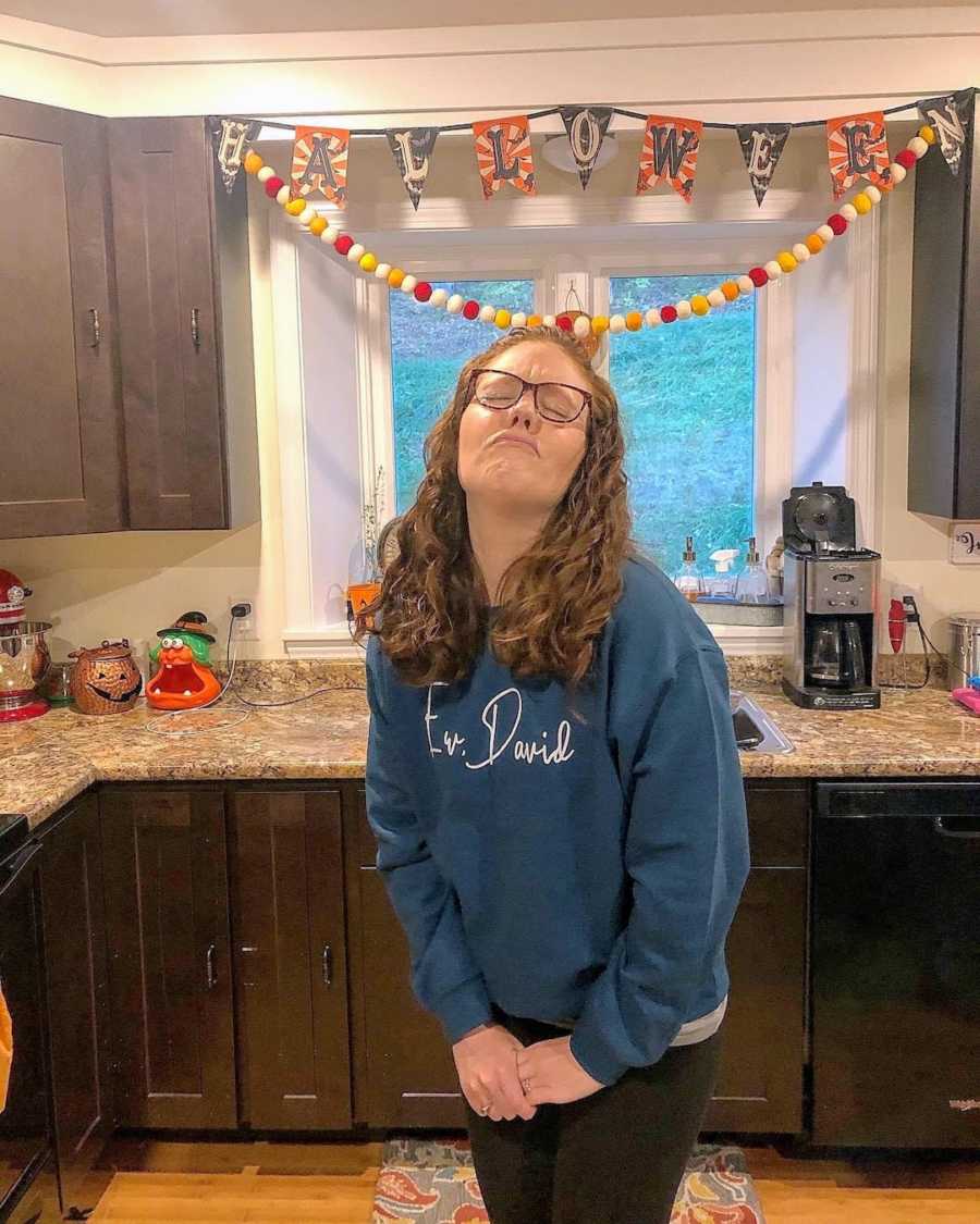 Woman wearing Schitt's Creek sweatshirt standing in kitchen with Halloween decorations