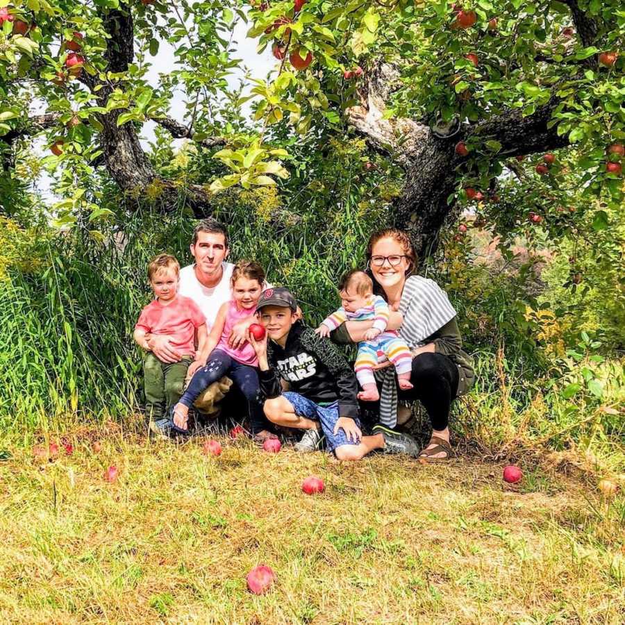 Family of 6 squatting outside by trees and grass and smiling