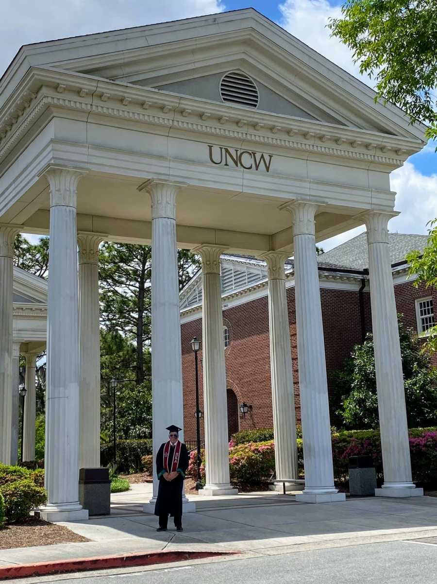 An older college graduate in cap and gown by pillars