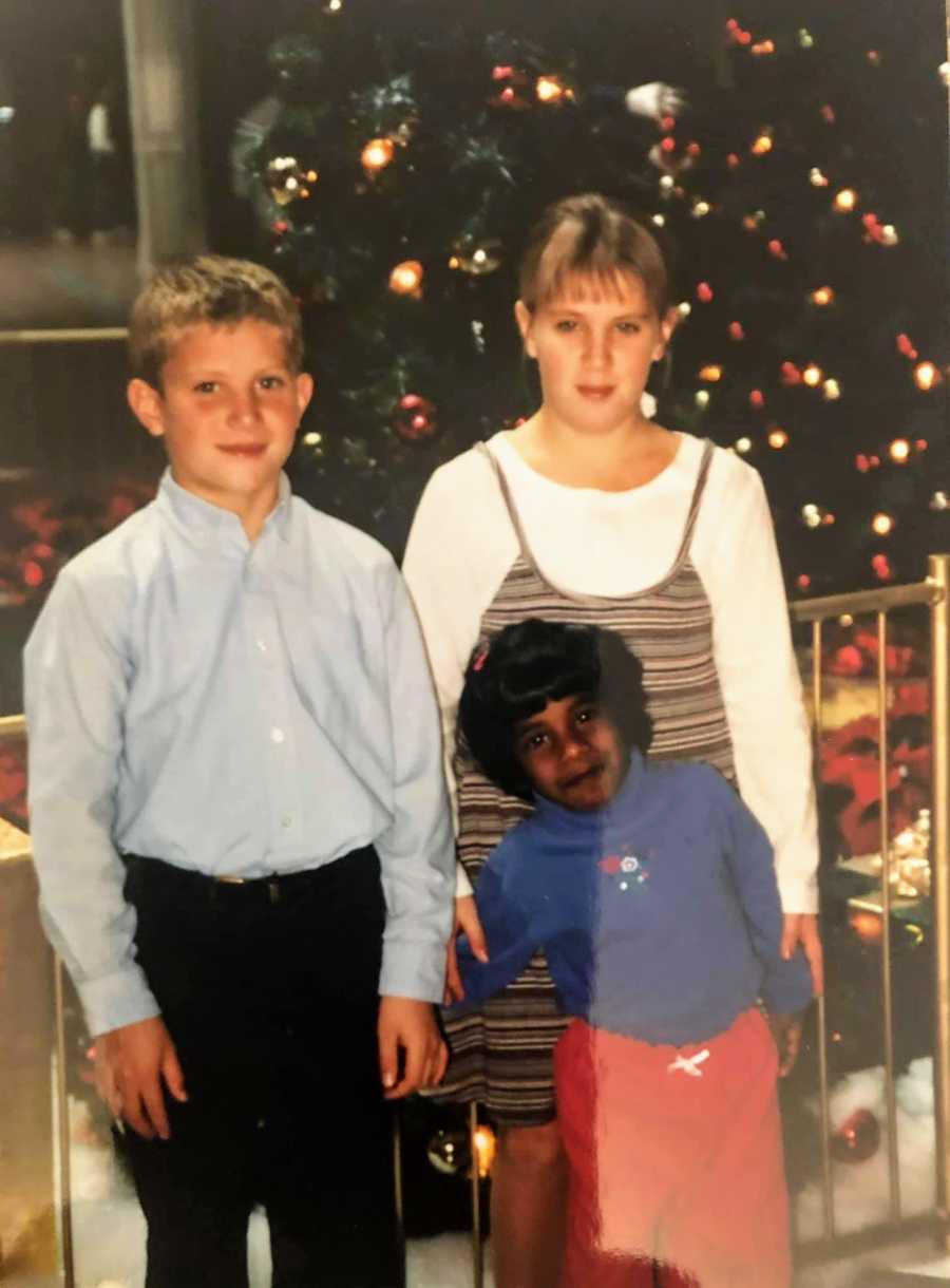 A transracial adopted child stands with her siblings by a Christmas tree