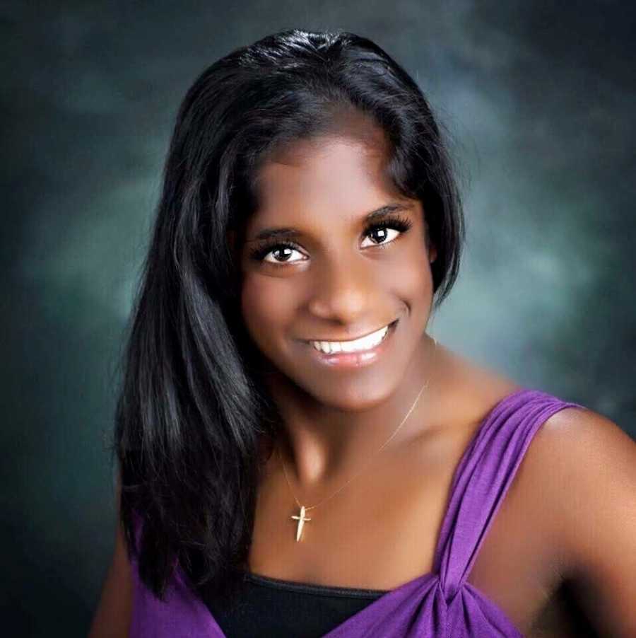 An Indian transracial adoptee wearing a purple shirt and cross necklace