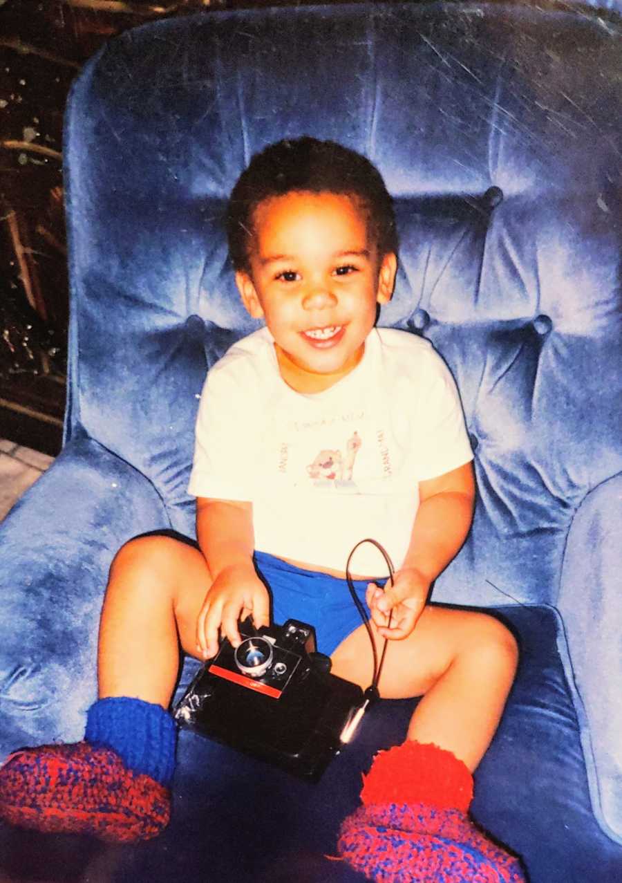 A mixed race adopted boy sits on a blue chair holding a camera