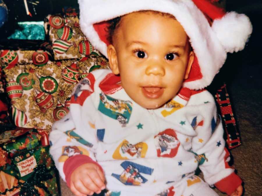 A mixed race adopted boy wearing a Santa hat and pajamas