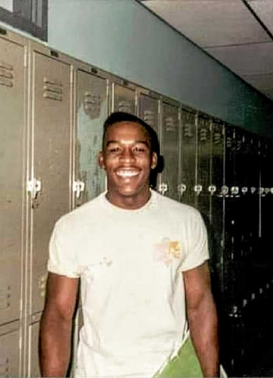 一个黑人少年站在学校的走廊里，身后是储物柜