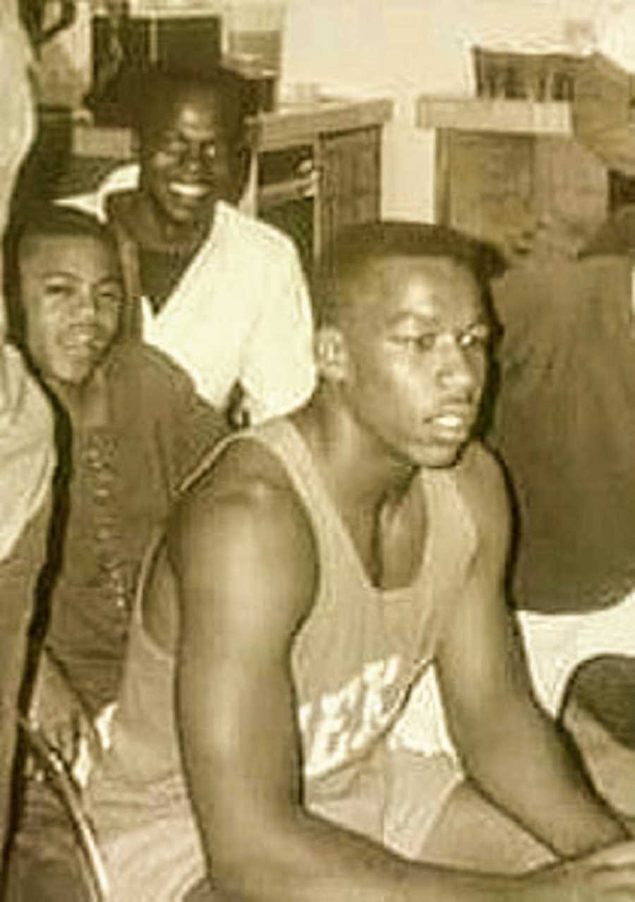 A Black teenager sits with others in a sports uniform