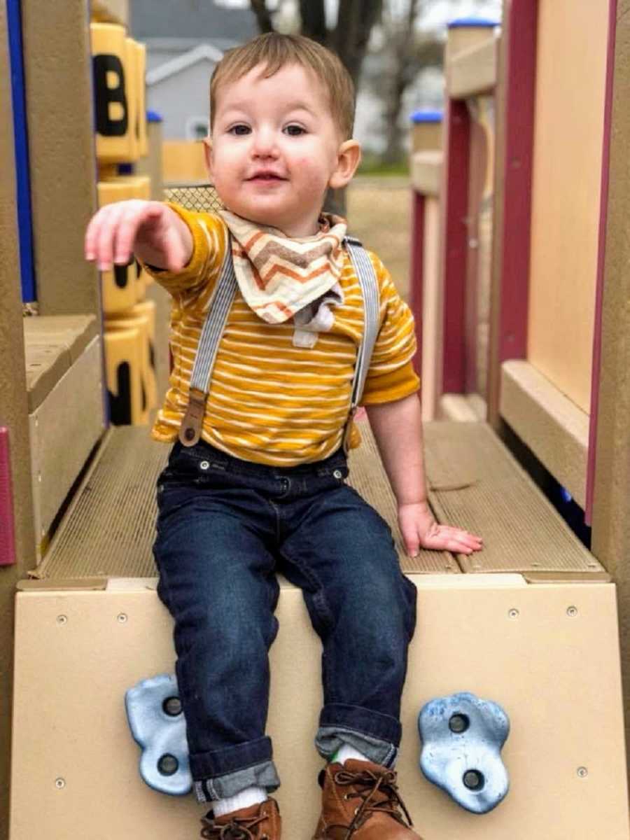 A two-year-old on a playground points at the camera