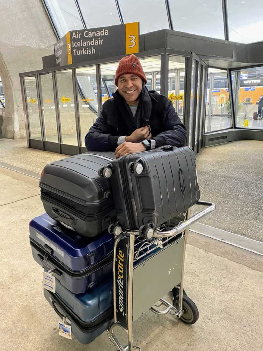 A man stands in an airport with a large pile of luggage