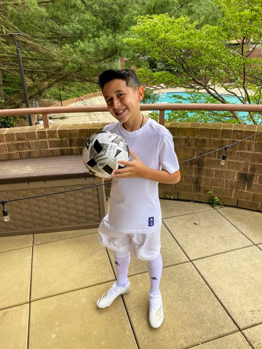 An adopted boy holds a soccer ball on an outdoor deck