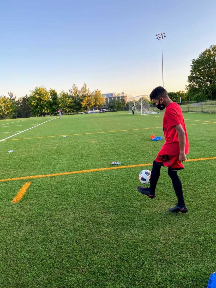 An adopted boy wearing red kicks a soccer ball