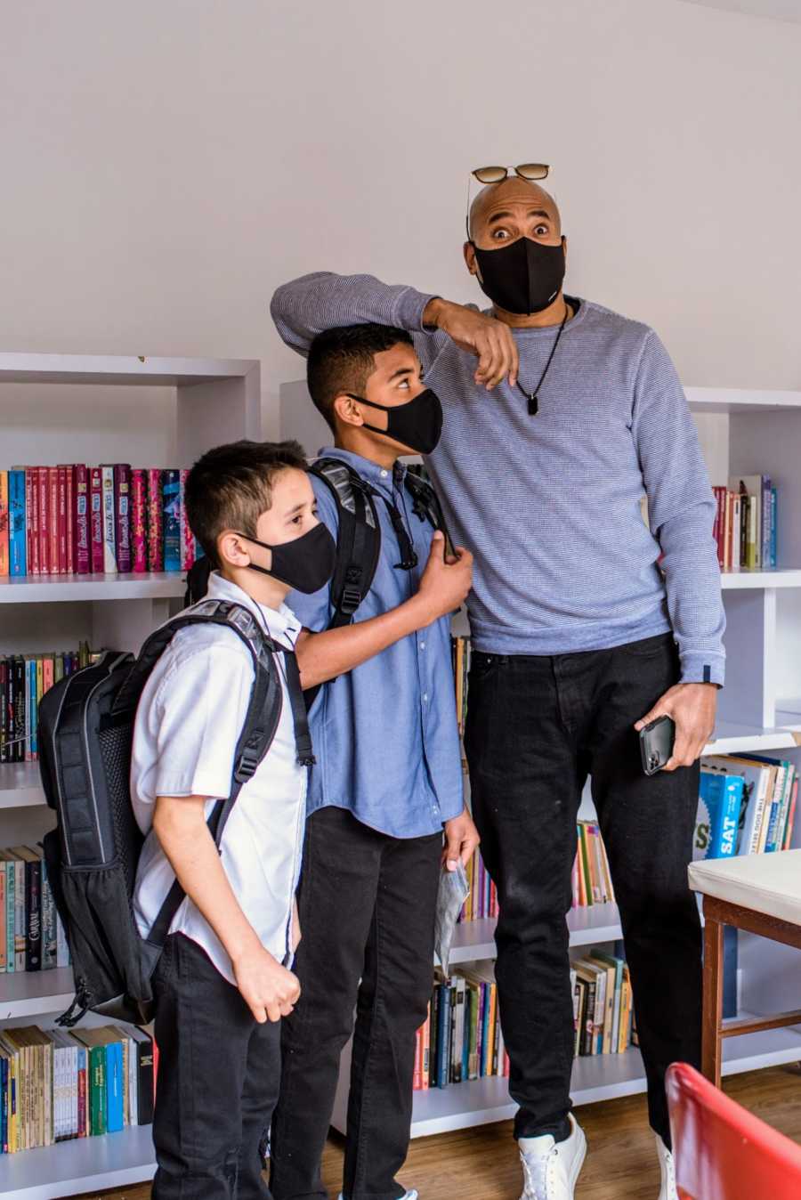 A pair of adopted brothers and their father stand by bookshelves