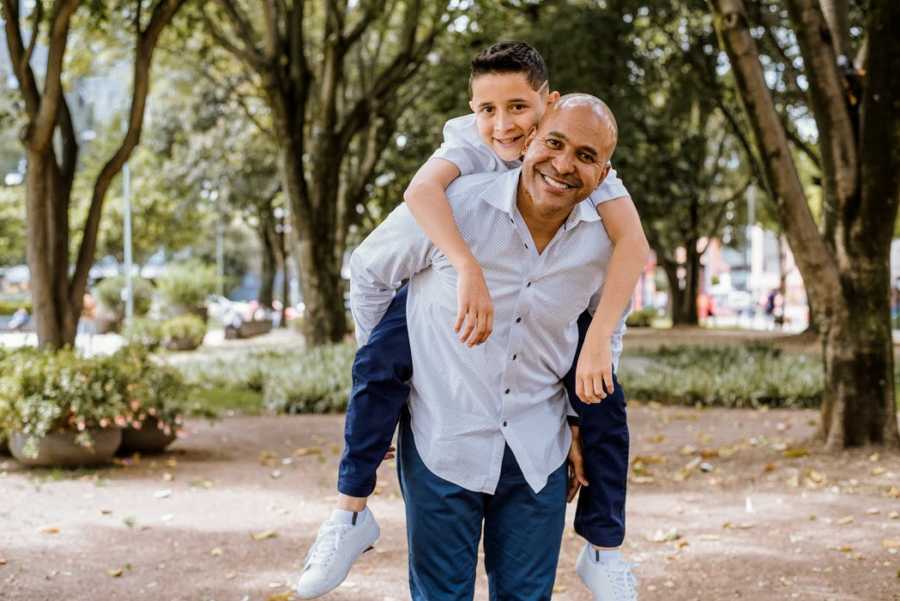 An adoptive father holds his son on his back