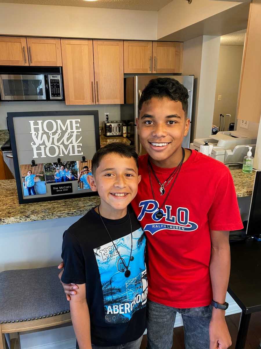 A pair of adopted brothers stand in a kitchen by a "Home Sweet Home" sign