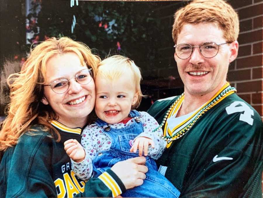 Mother and father holding baby daughter wearing green and smiling