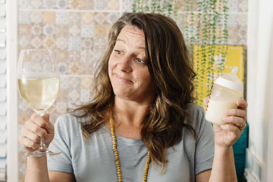 Woman holding wine glass and baby bottle looking at wine glass