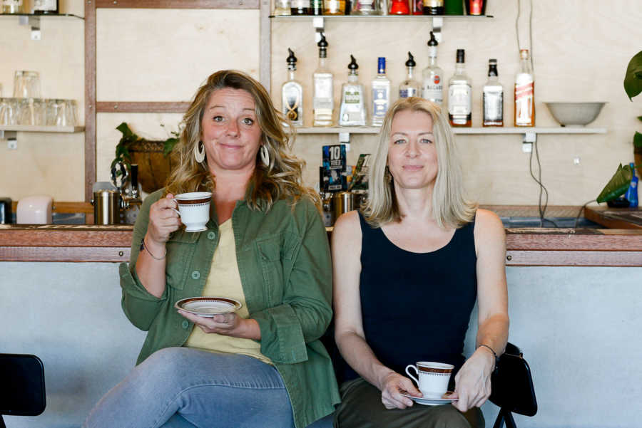 Two women sitting at the counter at a bar holding teacups