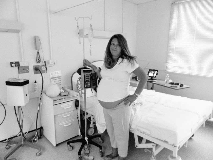 Pregnant woman with IV rack standing by hospital bed