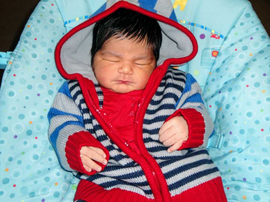 A baby boy sits wearing a striped sweater