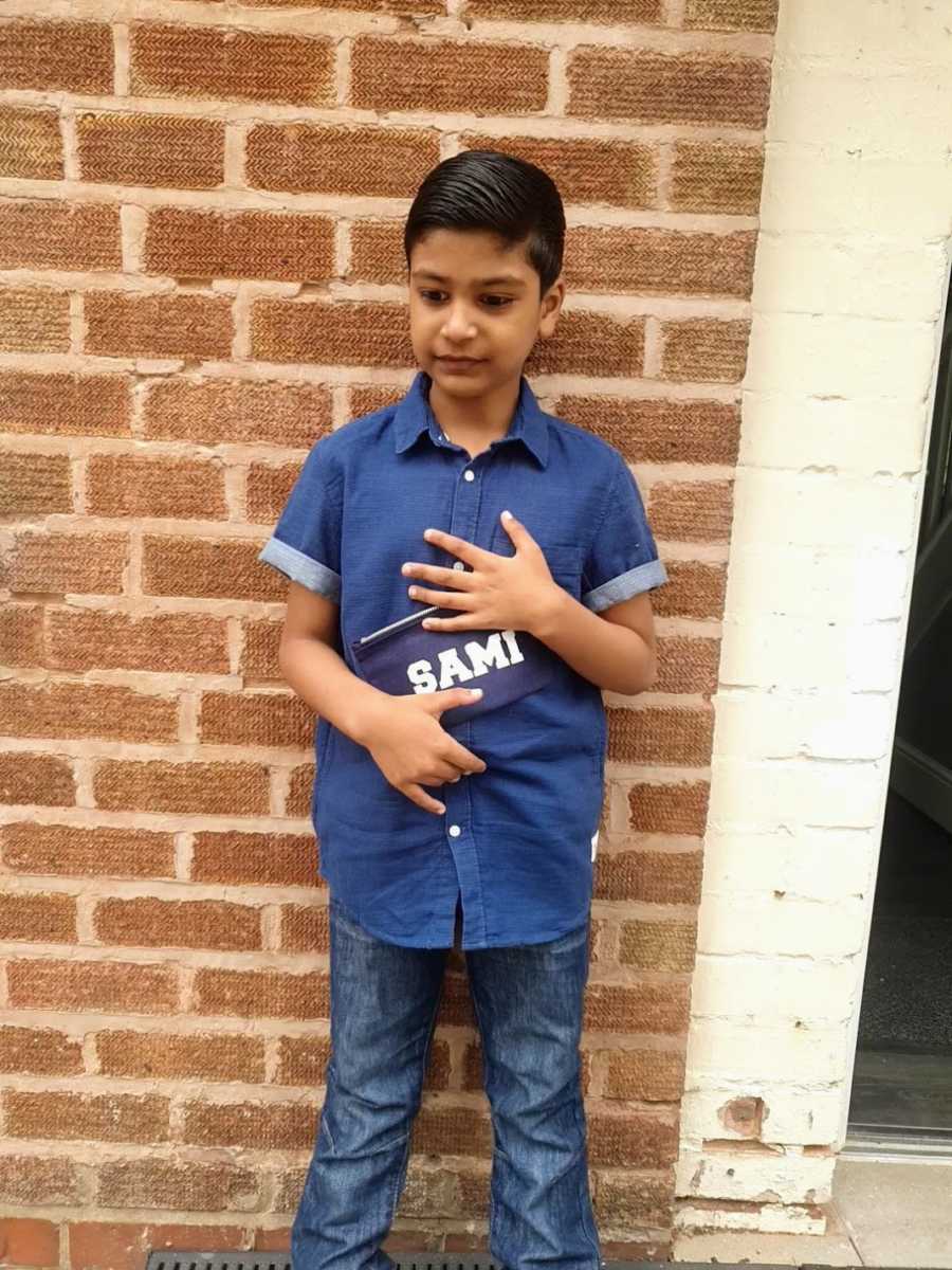 A boy with nonverbal autism stands against a wall holding a nametag