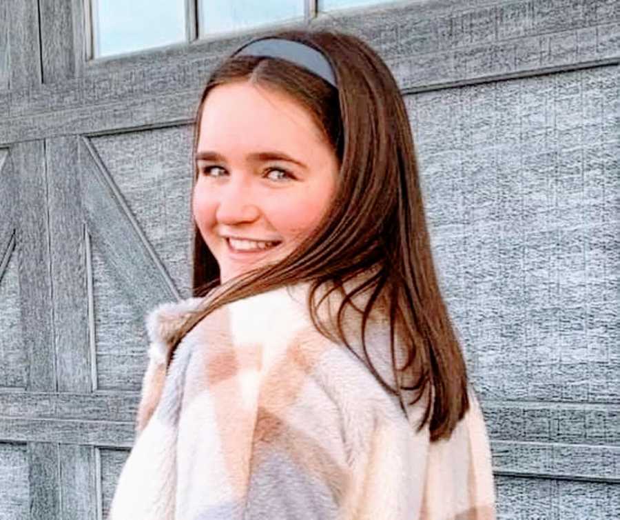 Young girl with gray headband and patterned jacket smiles at the camera