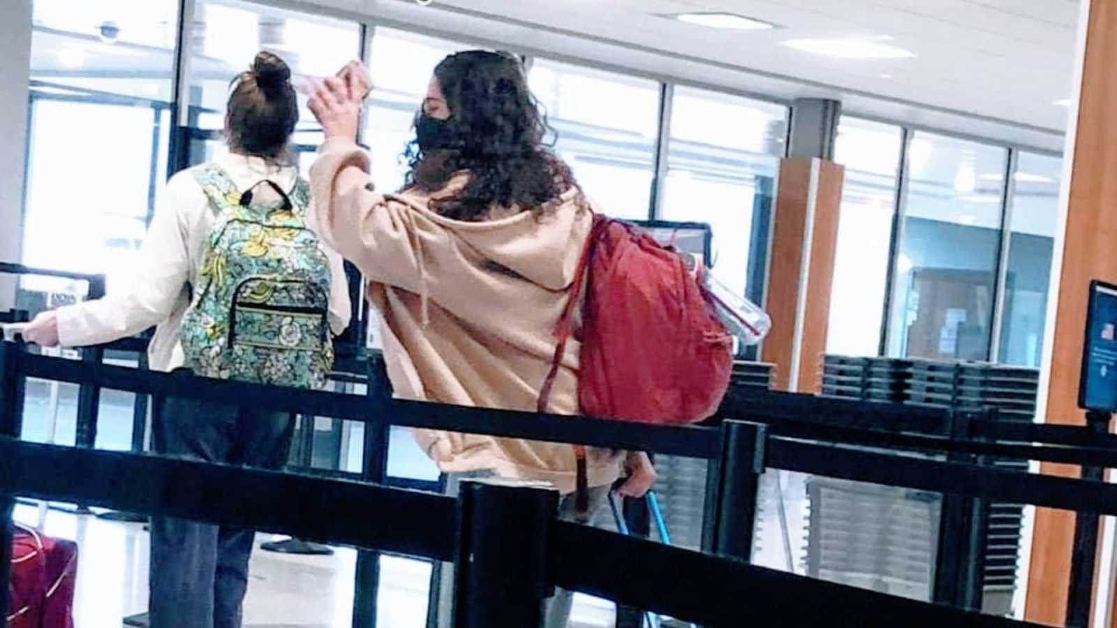 Daughter with a pink hoodie waves bye to her mom as she leaves to get on a plane