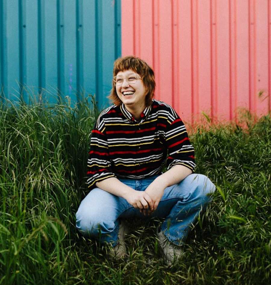 person outside crouching on grass in front of multi-color building