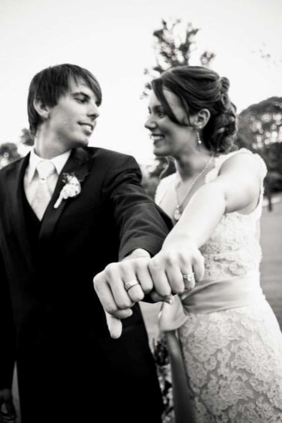 Newly weds smile at each other and show off their wedding rings