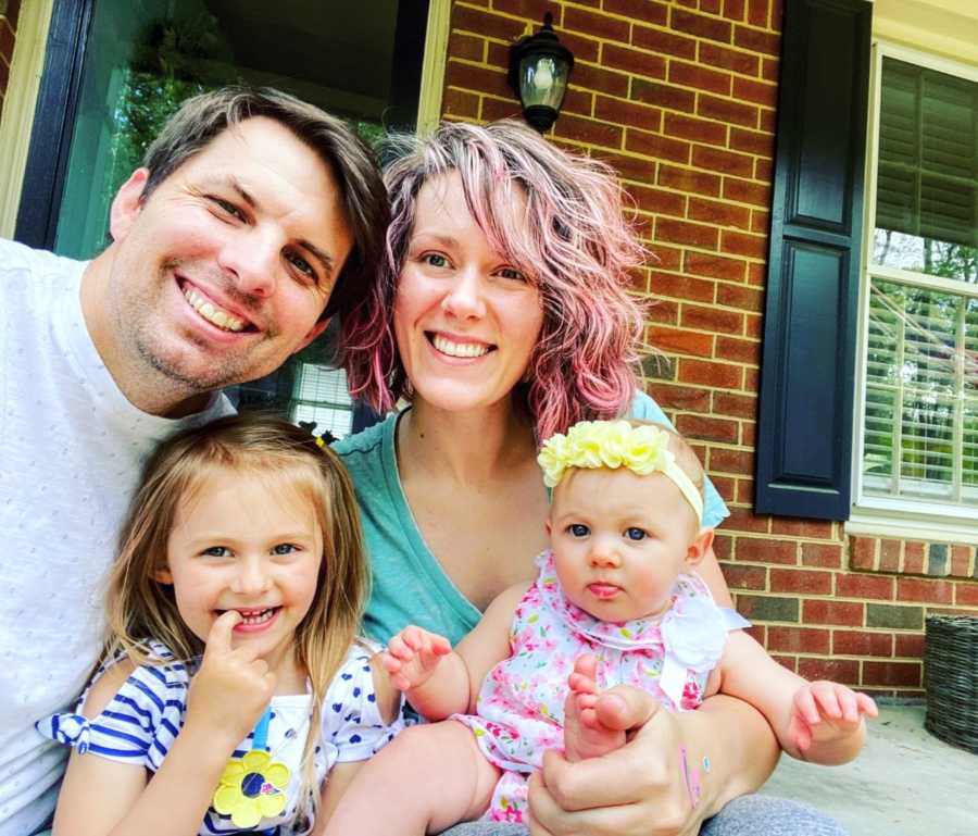 Young married couple take a selfie on their front porch with their two young daughters