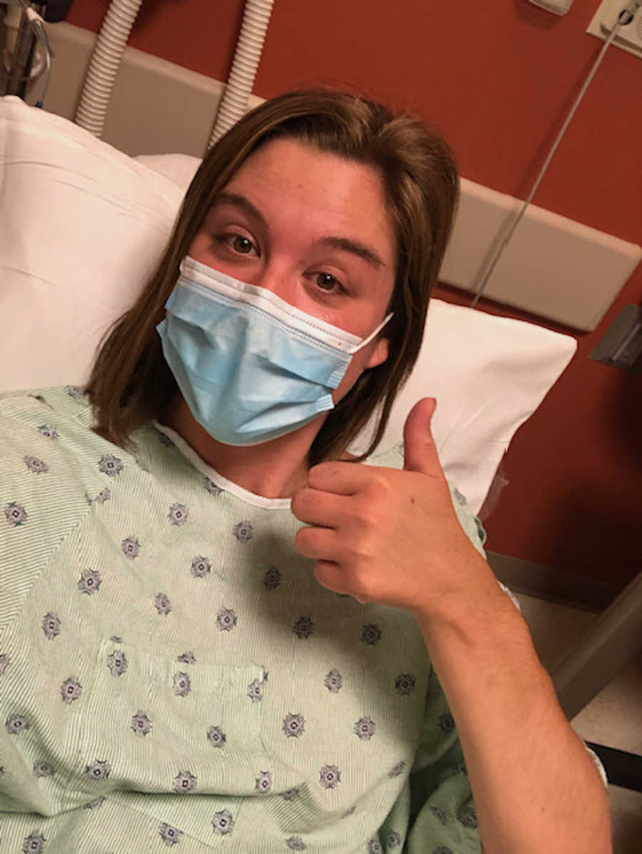 woman in hospital gown and mask giving thumbs up