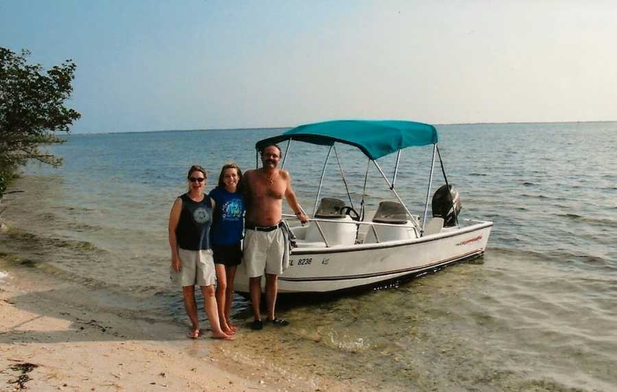 Mother and father with arms around daughter at beach with rented boat