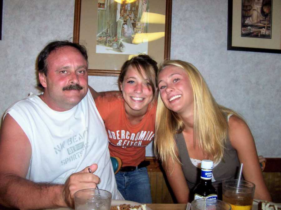 Father with arms around two daughters sitting in kitchen at dinner table