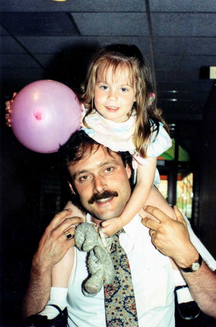 Father holding daughter on shoulders and the daughter is holding a pink balloon