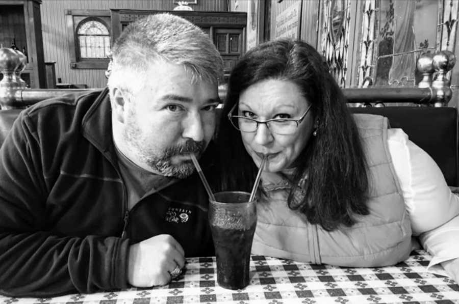 Woman sits in an old-fashioned diner and shares a coke with her husband