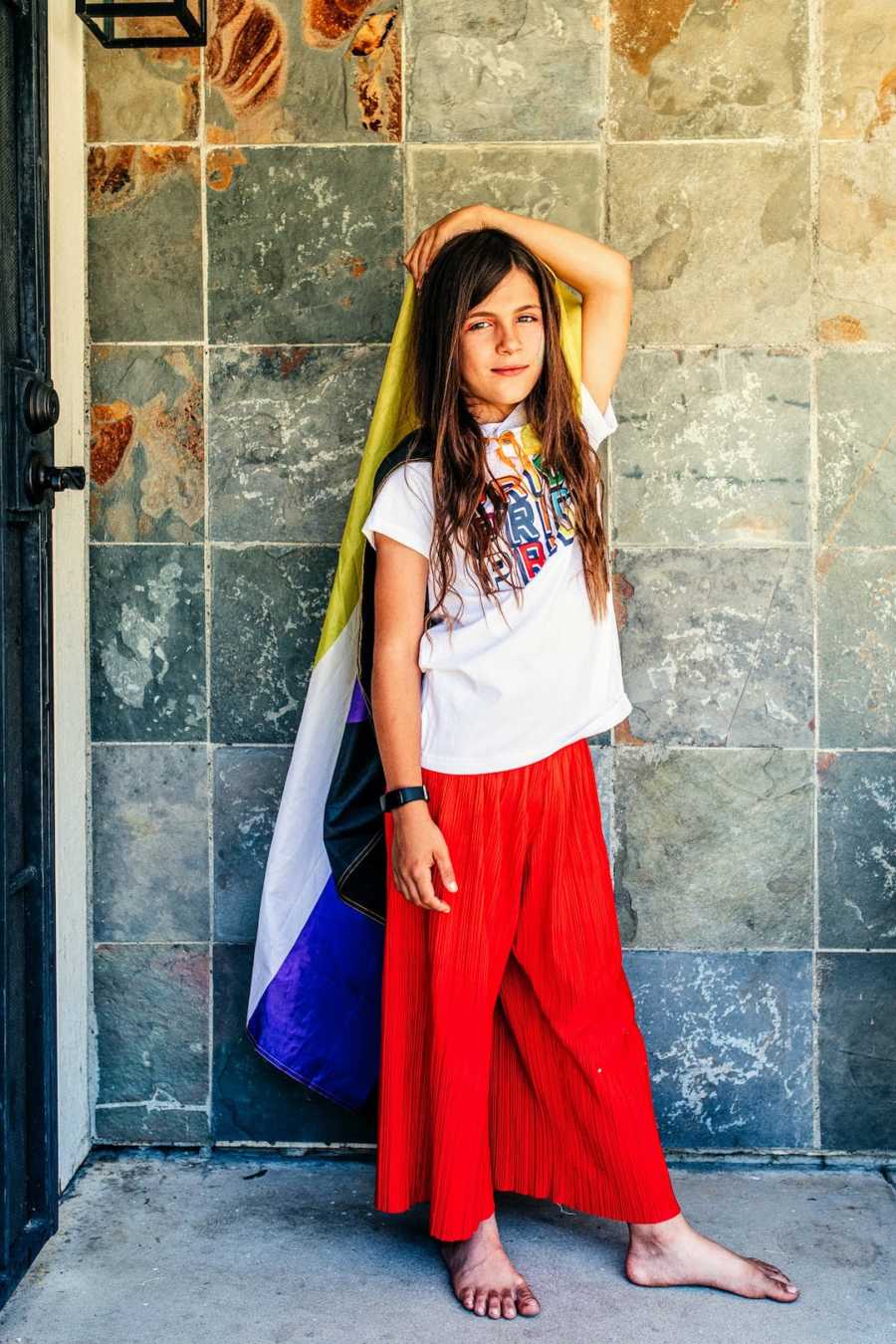 Child wearing rainbow colors and Pride shirt posing in front of stone wall