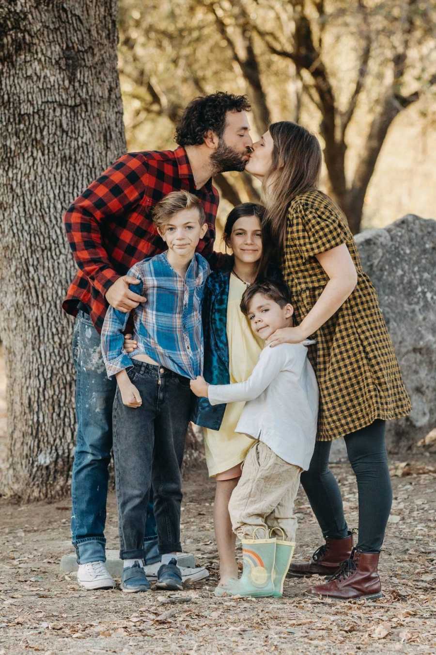 Family of five with children in front and parents kissing behind them