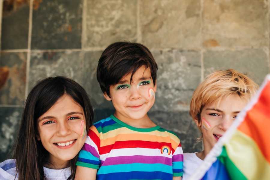 Three siblings celebrating Pride wearing rainbow colors and holding the Pride flag