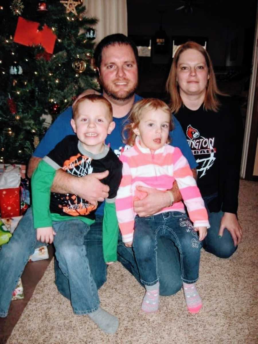 Couple pose with their son and daughter in front of a Christmas tree