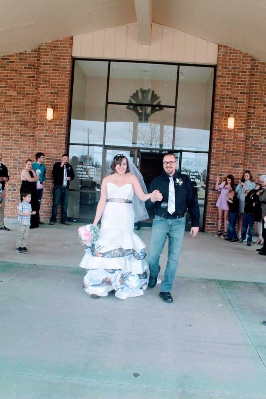 Newly weds walk out of their wedding reception hand-in-hand with big smiles