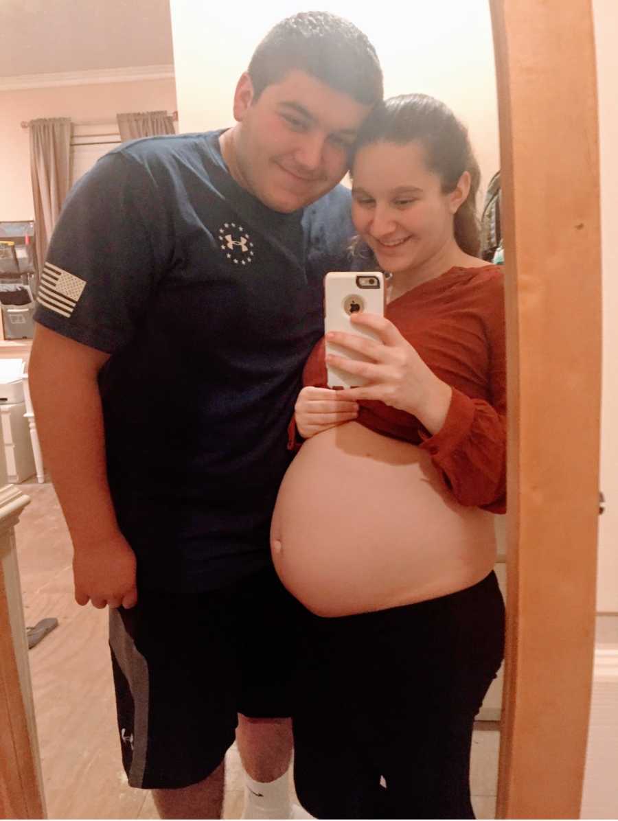 Two sixteen-year-olds expecting their first child together take a mirror selfie, showing off the mother's baby bump
