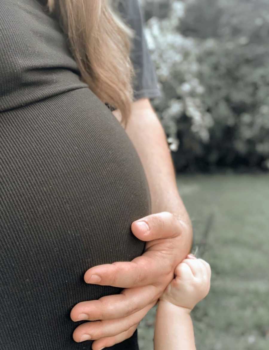 Young mom take a photo of her baby bump while her young daughter lays her hand on her stomach