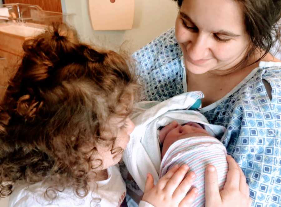 Young mom takes photo of her first daughter meeting her newborn daughter in the hospital