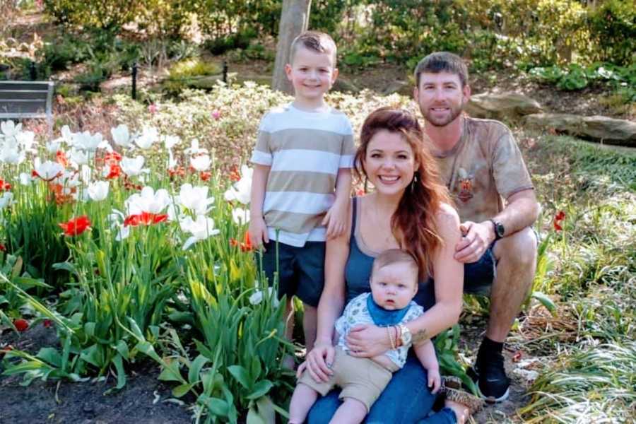 Family of four snap a beautiful photo sitting next to a field of white and red flowers