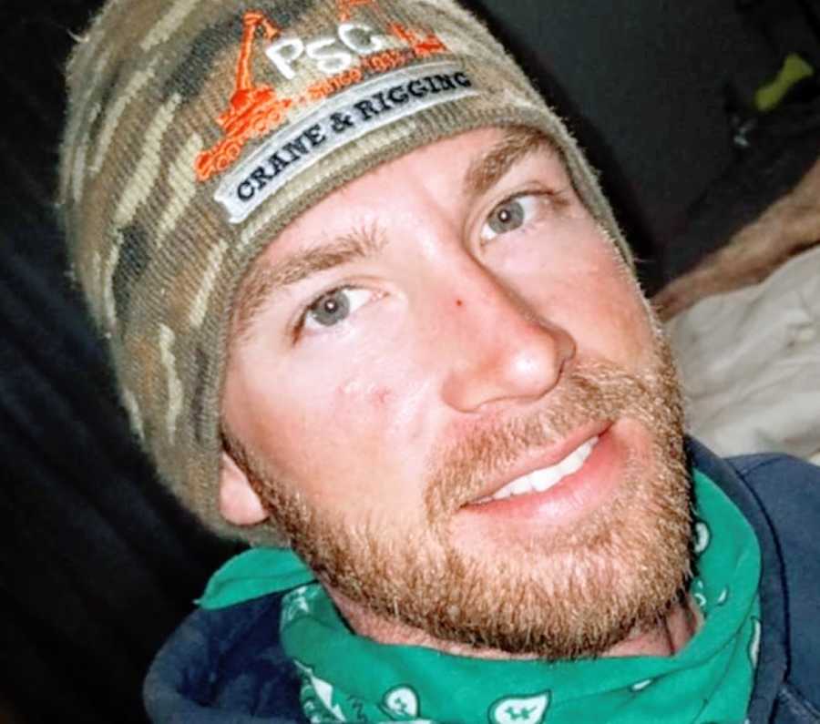 Man with a green bandana and a camo hat smiles for a photo
