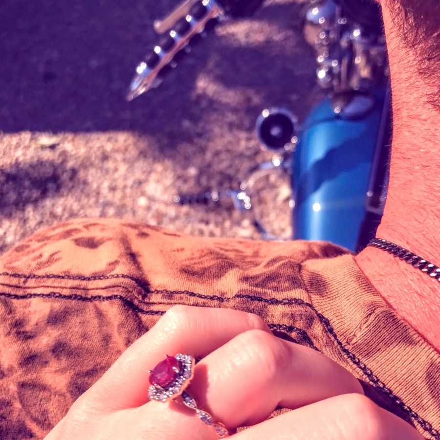 Woman shows off her beautiful ruby and diamond engagement ring while riding on the back of her fiancé's motorcycle