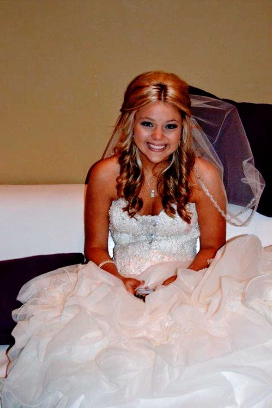 Woman sits on the floor and smiles in her wedding dress