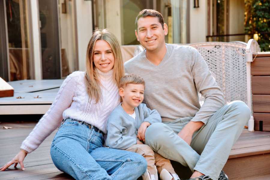 Family of three take a beautiful family photo in light fall weather on their back porch