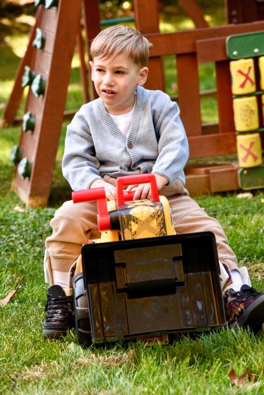 Young boy in gray sweater sits on a toy truck outside on a playground